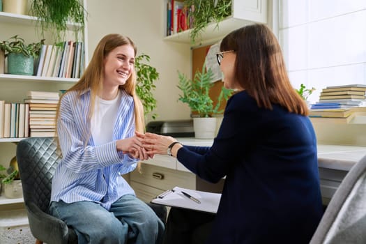 Smiling positive young teen female patient talking to professional mental therapist. Teenager girl high school college student in therapy with psychologist psychotherapist counselor. Treatment support