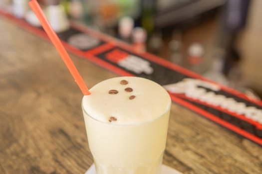 A cold coffee cocktail in a clear glass with a straw on a wooden bar counter.