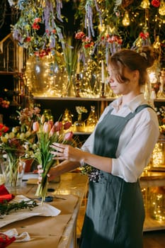 A woman in her florist shop collects bouquets of flowers. The concept of a small business. Bouquets of tulips for the holiday on March 8