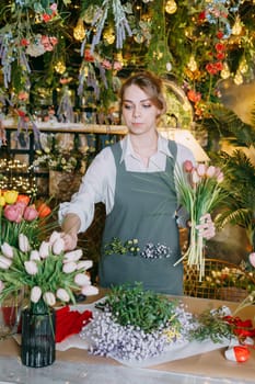 A woman in her florist shop collects bouquets of flowers. The concept of a small business. Bouquets of tulips for the holiday on March 8