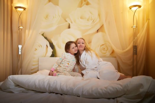 Mother and daughter happily relax and fun together on bed in bedroom. The concept of tenderness between mom and girl