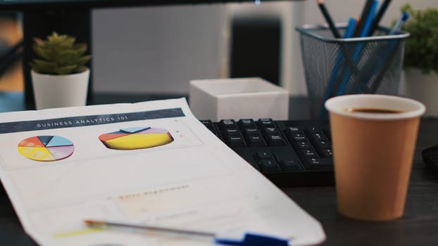 Financial report on desk next to paper cup of coffee in empty office, close up shot. Company files containing economic graphs and pie charts near hot beverage on table in workspace