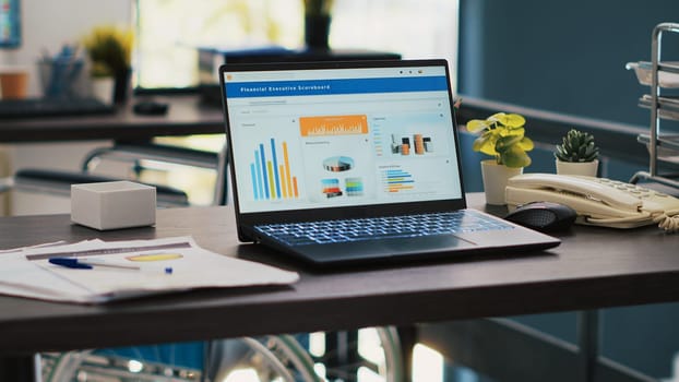 Inclusive office with wheelchair in blurry background and notebook in foreground showing marketing report. Workspace offering accessibility for workers and laptop with business analytics, panning shot