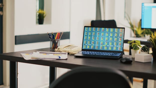 Laptop in company office shows stock exchange values changing in real time, panning shot. Paperwork on desk next to notebook showing forex trading indexes and pie charts graphs