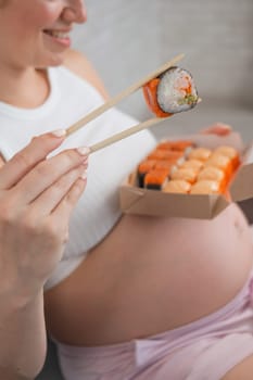 A pregnant woman sits on the sofa and eats rolls from a box. Food delivery