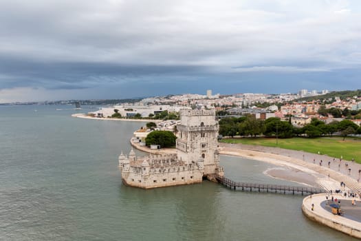 Aerial drone shot of Belem Tower overlooking cityscape. Fortress monument in Lisbon on Tagus River. 16th-century fortification Torre de Belem in city under cloudy sky. Evening time