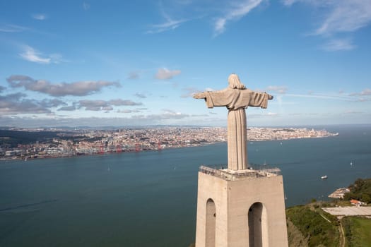Aerial view monument Sanctuary of Christ the King. Majestic scenery statue with cityscape Almada and Tagus Riverin background. Bird's eye view Catholic monument and city