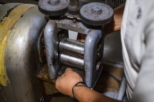 Skilled male worker performing precision manual labor by operating heavy industrial machinery in a manufacturing factory workshop to adjust gears and maintain equipment for safe and efficient production