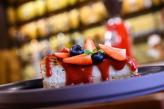 A delicious cheesecake topped with strawberries, blueberries, and coulis served on a plate
