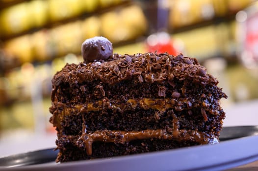Close-up view of a rich chocolate layer cake with hazelnut garnish in a bakery setting