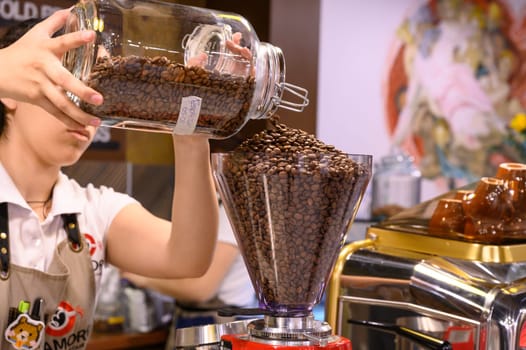 Barista refills a coffee grinder with fresh beans at a cafe