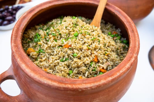 Clay pot with peruvian Arroz con Pollo, which is made of rice, chicken parts, peas, corn, aji hot pepper and cilantro