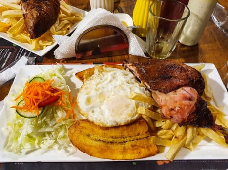 Close-up view of a latin american meal with grilled meat, plantains, fries, and egg, served on a white plate