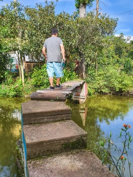 Adult male approaches a rustic wooden bridge across a tranquil pond surrounded by lush greenery