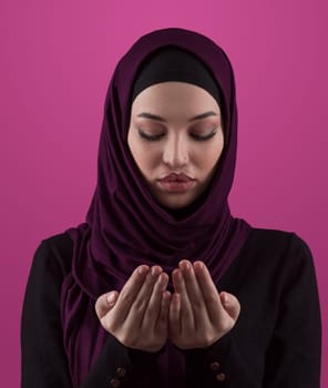 Muslim woman in hijab and traditional clothes praying for Allah, copy space. Muslim woman with hijab praying indoor pink background. High quality photo