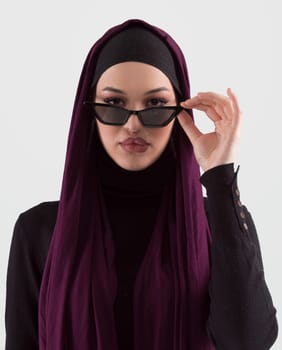 Portrait of beautiful stylish young muslim woman wearing black hijab and sunglasses as modern eastern fashion concept posing on white background. High quality photo