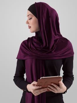 Beautiful and modern young Arabic businesswoman in hijab using a tablet computer while posing on light background and smiling at the camera. Business diversity concept, Muslim lady. High quality photo