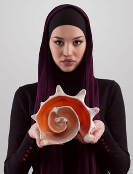 Pretty stylish Muslim woman wearing hijab and holding a seashell and dreams closed eyes. Golden ratio and ideal proportion concept.High quality photo