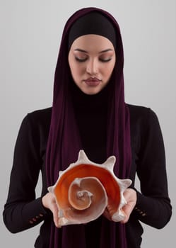 Pretty stylish Muslim woman wearing hijab and holding a seashell and dreams closed eyes. Golden ratio and ideal proportion concept.High quality photo
