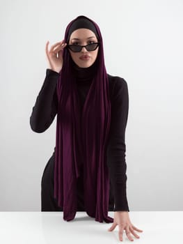 Portrait of beautiful stylish young muslim woman wearing black hijab and sunglasses as modern eastern fashion concept posing on white background. High quality photo