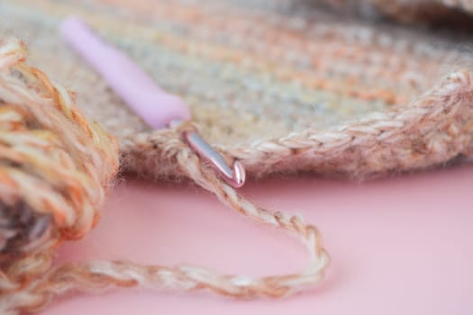 Closeup of a crochet hook and wool yarn on a magenta surface.