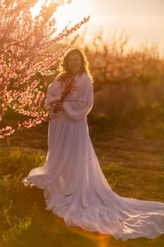 Woman blooming peach orchard. Against the backdrop of a picturesque peach orchard, a woman in a long white dress enjoys a peaceful walk in the park, surrounded by the beauty of nature