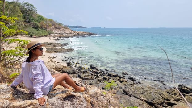 Koh Samet Island Thailand, Asian Thai women sitting on a rock looking out over the bay with a tropical beach and a blue ocean