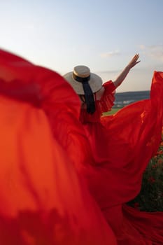 Woman poppy field red dress hat. Happy woman in a long red dress in a beautiful large poppy field. Blond stands with her back posing on a large field of red poppies