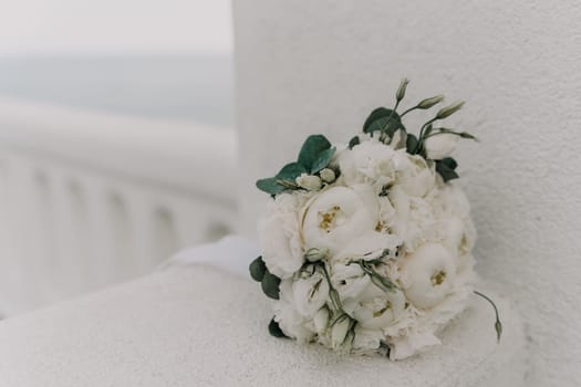 A white bouquet of flowers sits on a white wall. The flowers are white and green, and they are arranged in a vase. The vase is placed on a ledge, and the bouquet is the main focus of the image