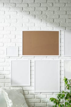 Several empty photo frames of different sizes and colors are displayed in an asymmetrical arrangement against a textured white brick wall, potentially signifying a modern and minimalist interior design approach. A small portion of a green plant is visible, injecting a touch of nature into the scene.