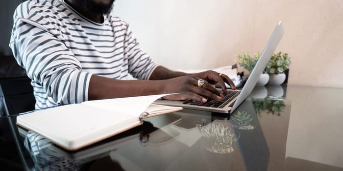 Close up of black man hands typing on a laptop work from home sitting on a desk.