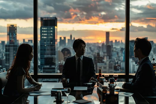 Three people are sitting at a table in a city, with a sunset in the background. They are dressed in business attire and appear to be discussing something important
