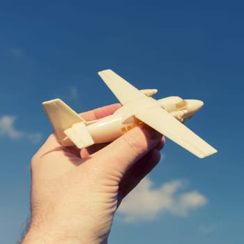 close up photo of male hand holding toy airplane against blue sky . image is retro filtered
