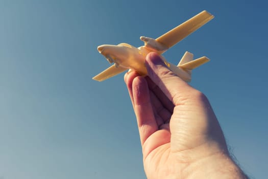 close up photo of male hand holding toy airplane against blue sky . image is retro filtered