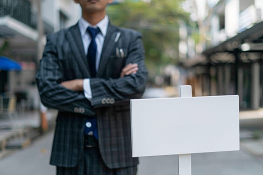 Real Estate agency in a suit stands in front empty sign board.