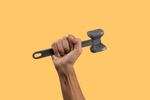 Black male hand holding a kitchen hammer isolated on yellow background. High quality photo