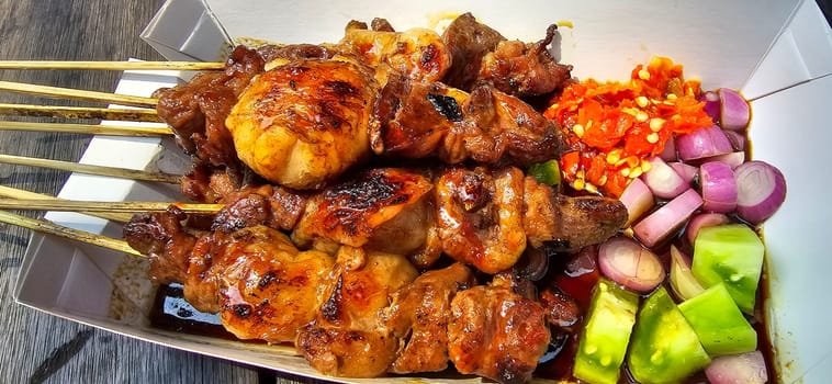 Lamb grilled satay served with barbecue savory sauce and pickled onion, chili and cucumber, selective focus photo on top of wooden table