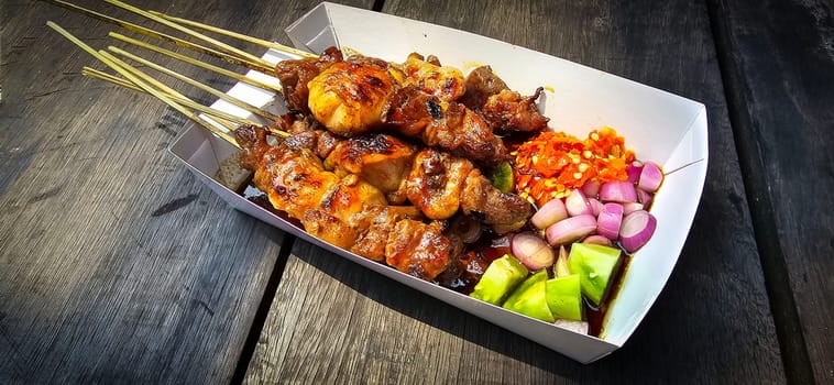 Lamb grilled satay served with barbecue savory sauce and pickled onion, chili and cucumber, selective focus photo on top of wooden table