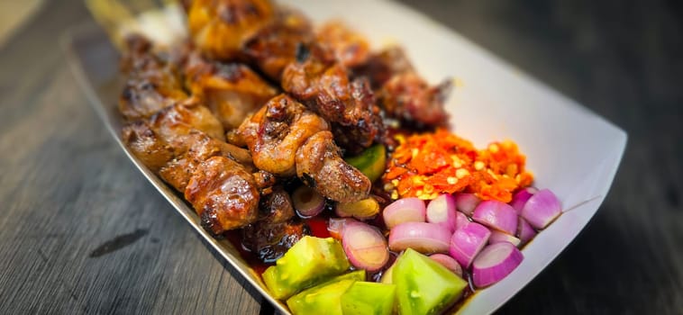 Lamb grilled satay served with barbecue savory sauce and pickled onion, chili and cucumber, selective focus photo on top of wooden table
