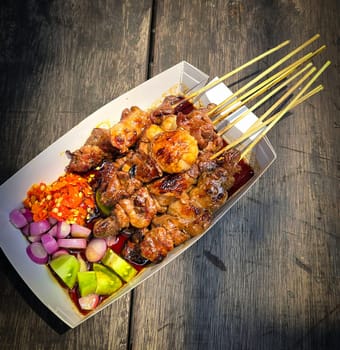 Lamb grilled satay served with barbecue savory sauce and pickled onion, chili and cucumber, selective focus photo on top of wooden table