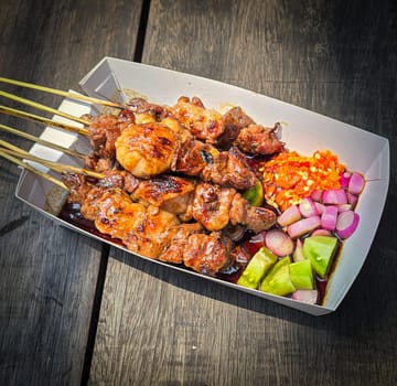 Lamb grilled satay served with barbecue savory sauce and pickled onion, chili and cucumber, selective focus photo on top of wooden table