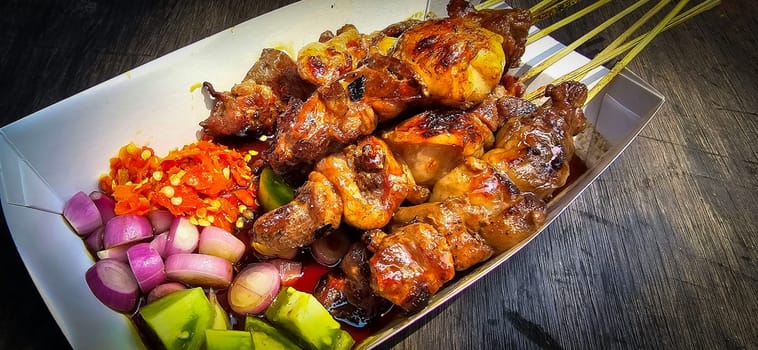 Lamb grilled satay served with barbecue savory sauce and pickled onion, chili and cucumber, selective focus photo on top of wooden table