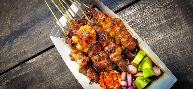 Lamb grilled satay served with barbecue savory sauce and pickled onion, chili and cucumber, selective focus photo on top of wooden table