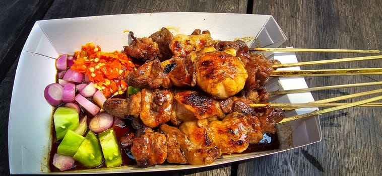 Lamb grilled satay served with barbecue savory sauce and pickled onion, chili and cucumber, selective focus photo on top of wooden table