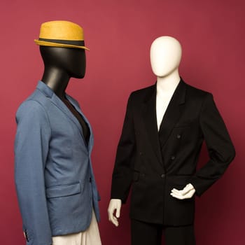 Two male mannequin in a black business suit and in a blue suit and white pants on a ruby background - image