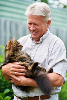 Elderly, man and love for cat is outdoors with care for pets, animals and furry childhood friend. Happy, male person and bonding with companion in backyard of house with kitten, embrace and garden.