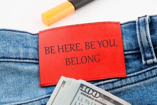 BE HERE, BE YOU, BELONG Words written on the leather insert of jeans with dollar bills sticking out