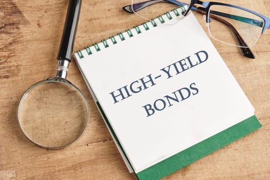 Inscription High-Yield Bonds on a notebook with a magnifying glass and glasses on a vintage background