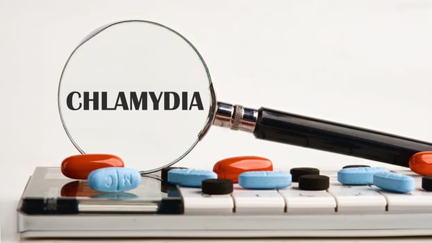 Medical concept. Word Chlamydia. through a magnifying glass on a light background on a calculator, about scattered pills, vitamins