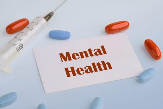 Health concept. Mental Health text on a white business card on a blue background next to a syringe, pills, vitamins